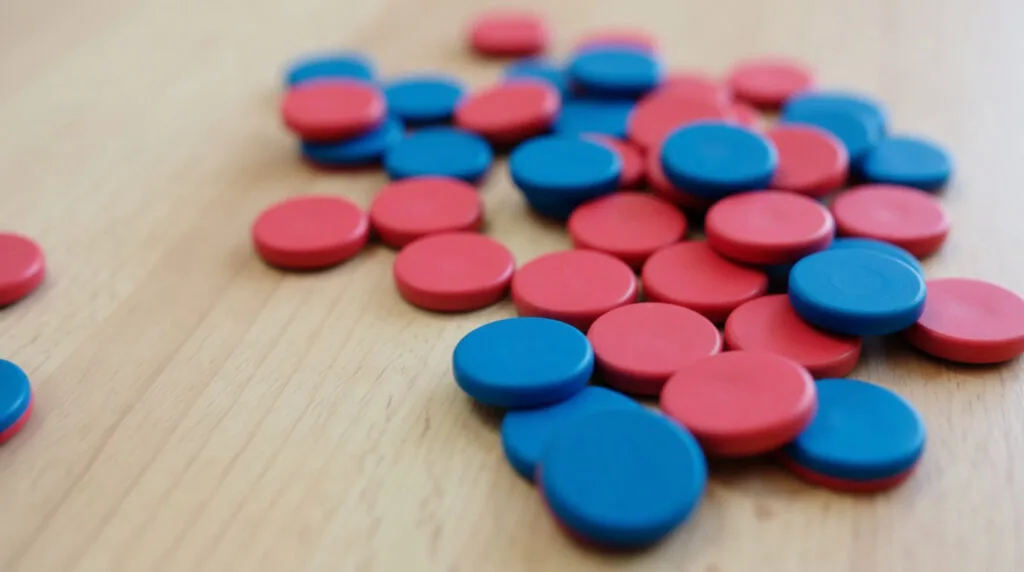 Vue rapprochée de nombreux jetons de comptage rouges et bleus dispersés sur une surface en bois clair, utilisés en éducation.
